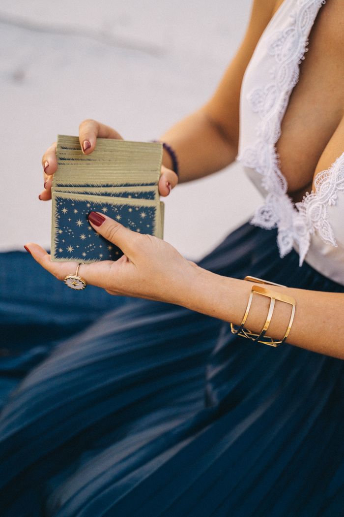Close-up of a woman's hands holding tarot cards, outdoors in a serene setting.
