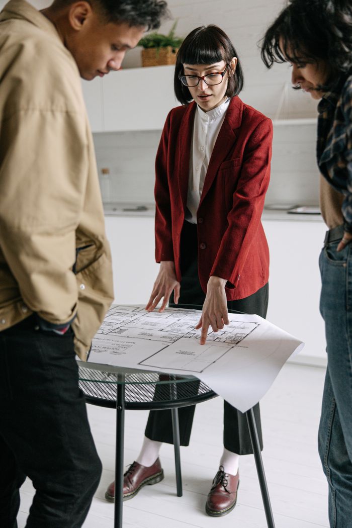 services-06 A real estate professional discusses architectural plans with clients in an office setting.