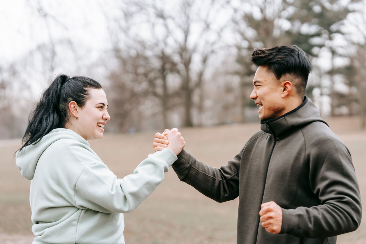 Side view of cheerful plus size female and ethnic instructor in activewear giving hands to each other on blurred background